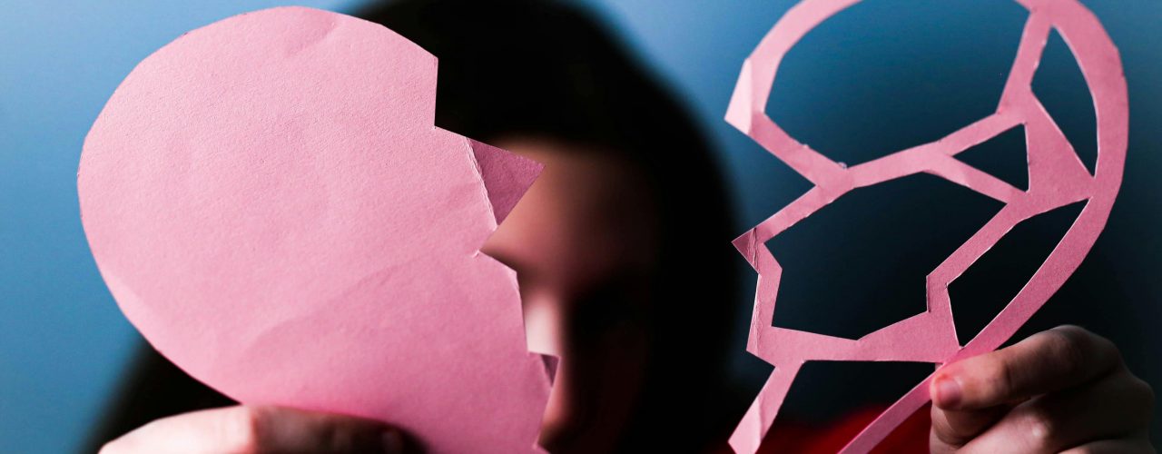 Femme tenant un cœur brisé en papier devant son visage, symbolisant une peine sentimentale